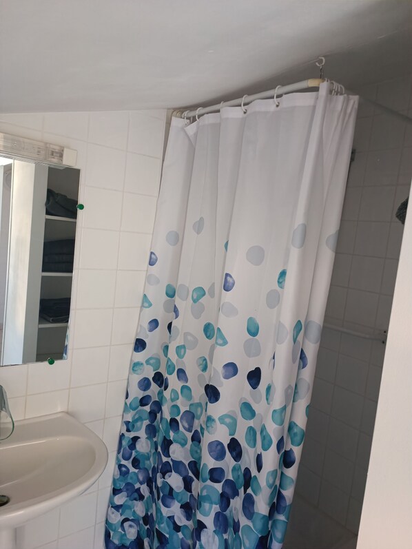 A bathroom with a white tiled wall, a white sink, and a shower curtain with a blue and white abstract pattern. - Camping les Lavandes (Castellane)