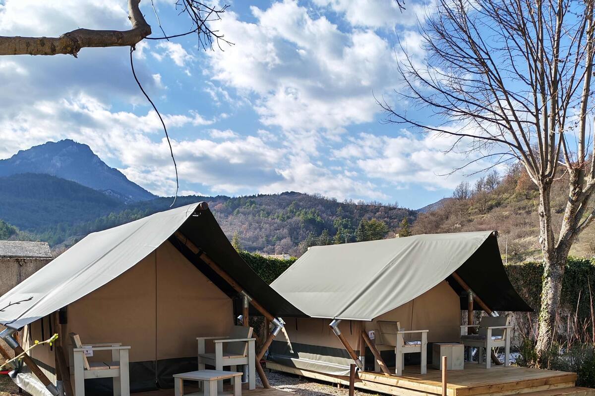 Two tents with wooden decks and seating, set against a mountainous backdrop.