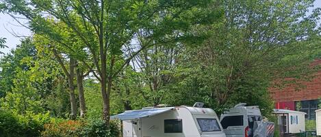 Een camping met campers tussen bomen en een klein gebouw.