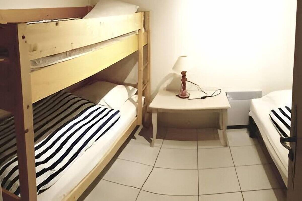 A small, clean room with two bunk beds, a bedside table with a lamp, and a tiled floor.