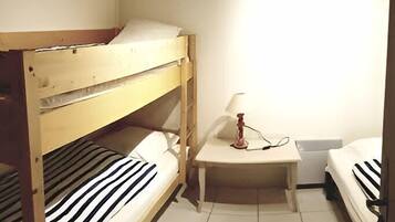 A small, clean room with two bunk beds, a bedside table with a lamp, and a tiled floor.