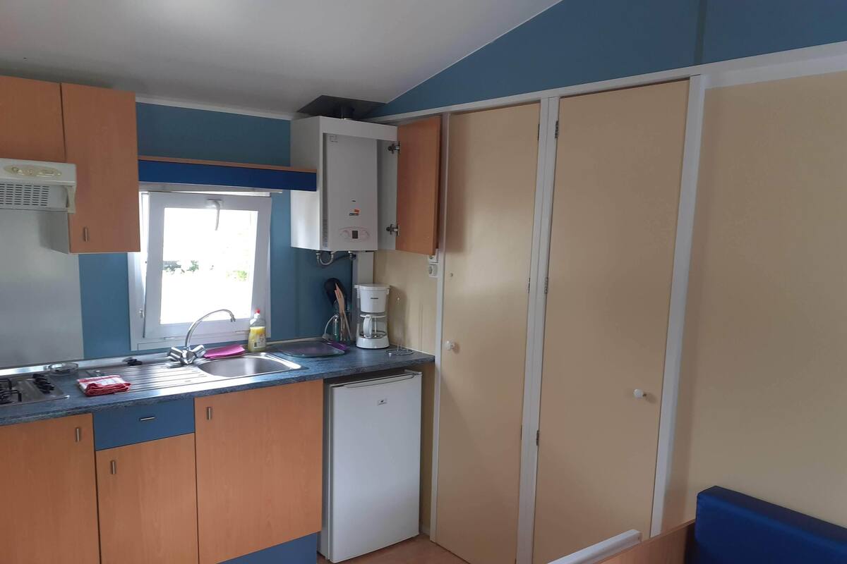 A compact kitchen with a sink, stove, and a coffee maker. There is a window providing natural light and a door leading to another room.