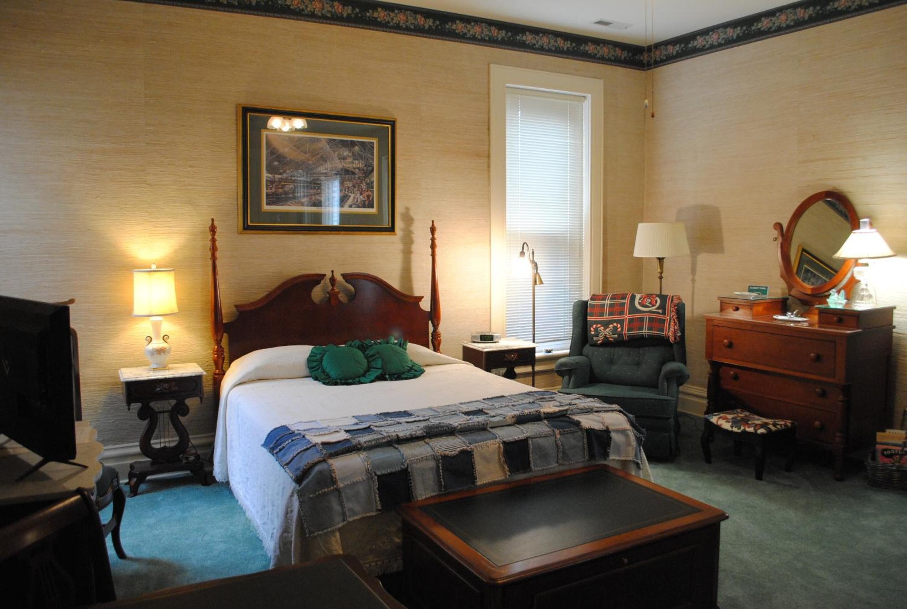 A hotel room with a bed, a chair, a dresser, a desk, and a lamp.
