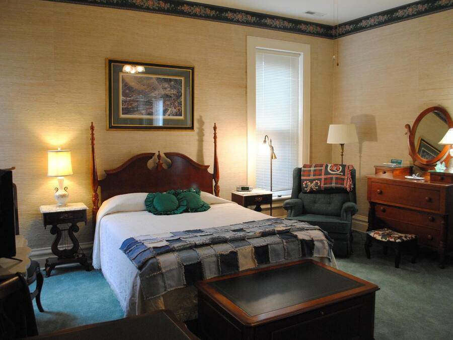 A hotel room with a bed, a chair, a dresser, a desk, and a lamp.