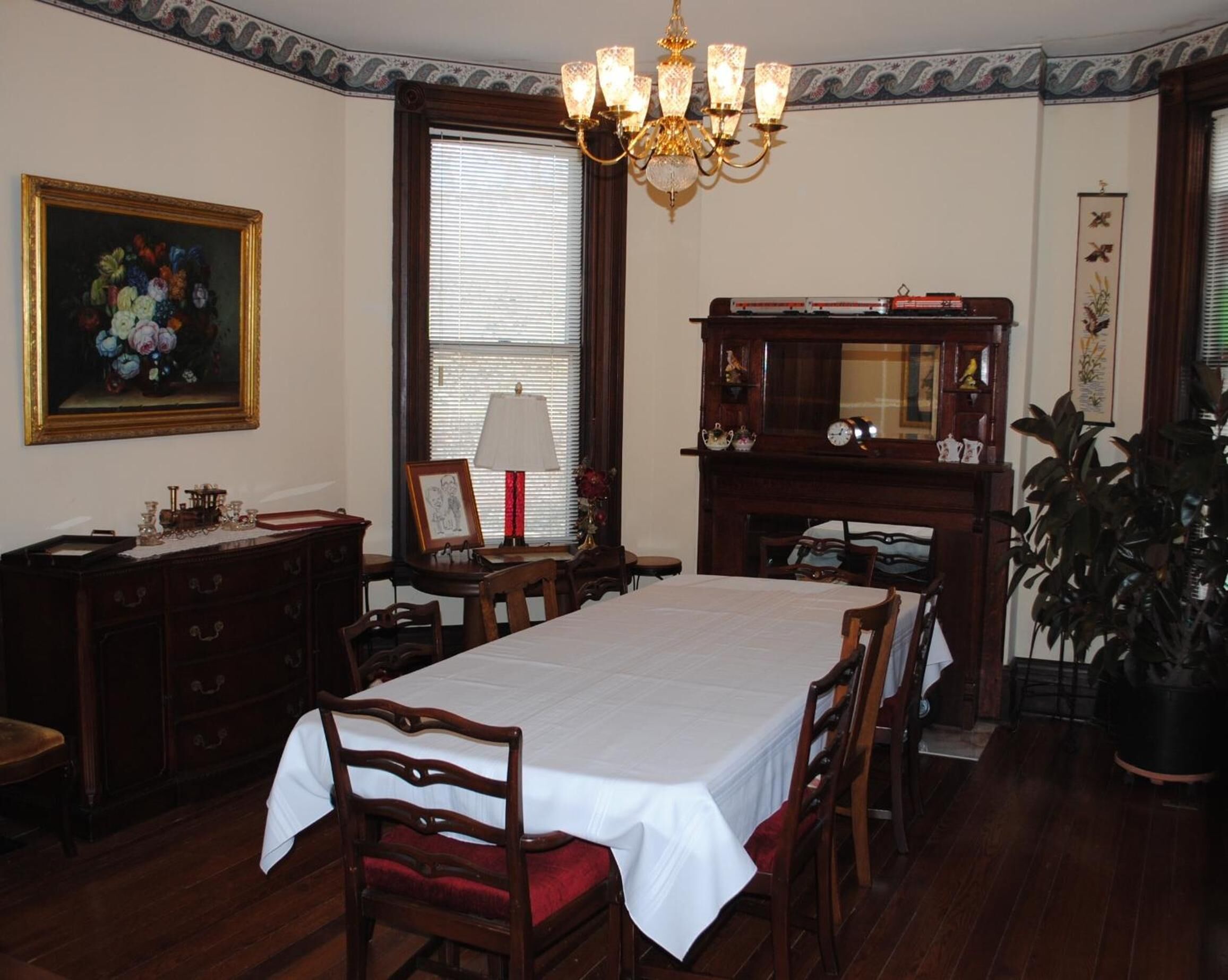 Ein Zimmer mit einem großen Esstisch, Holzsesseln, einer Chandelier, einem Kamin und einem Gemälde an der Wand.