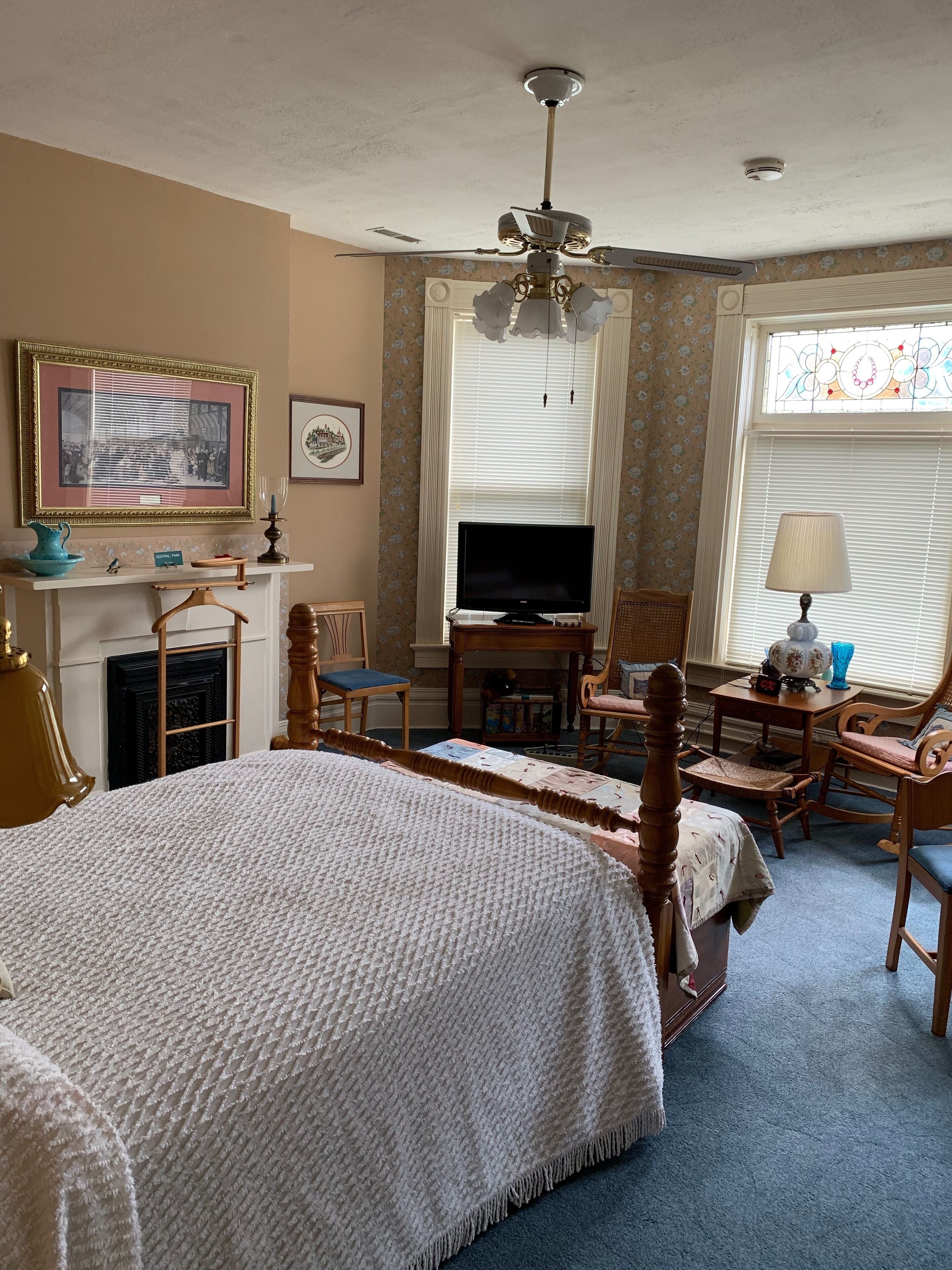 A hotel room with a large bed, a television, a fireplace, and a ceiling fan.