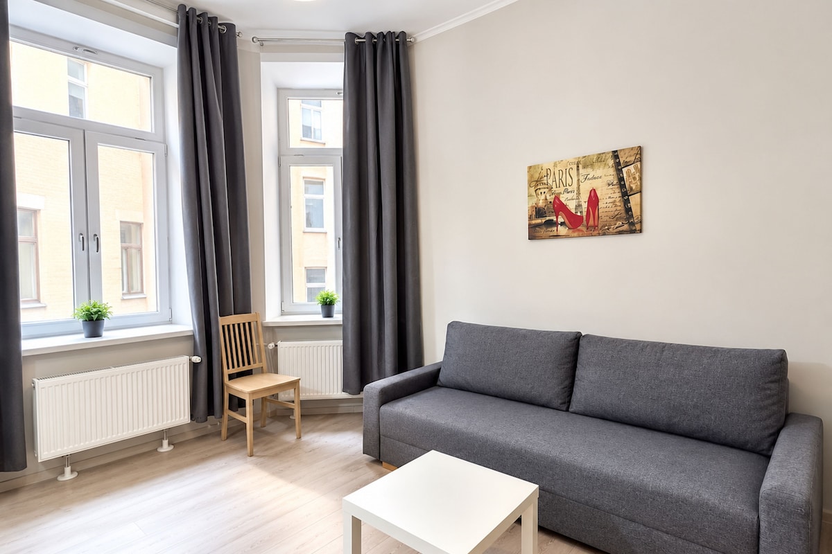 A modern living room with a grey sofa, a white coffee table, a wooden chair, and a radiator.