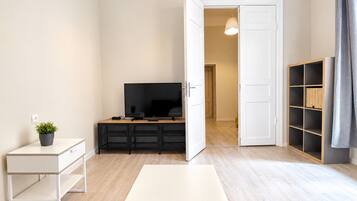 Ein minimalistisches Wohnzimmer mit Flachbildfernseher, einem kleinen Tisch und einem Bücherregal.
