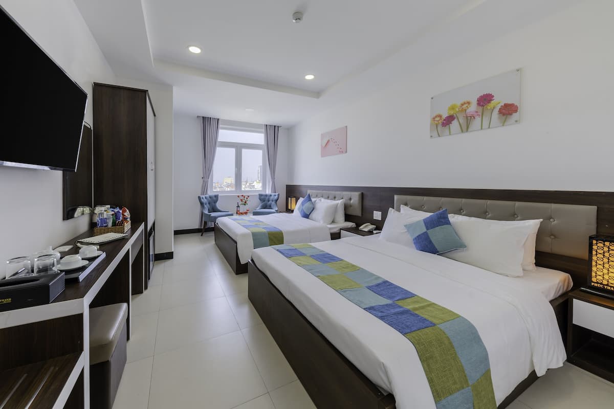 A hotel room with two beds, a desk with a flat-screen TV, a window with curtains, and a wall-mounted artwork of flowers.