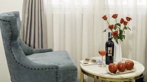 A room with a blue upholstered chair, a small round table with a bottle of wine, a glass of wine, a vase with red roses, and a plate with apples. - Phuc Thanh Hotel (Da Nang)