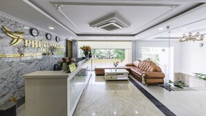 A hotel reception area with a marble reception desk, a brown leather sofa, a coffee table, and a large window offering a view of greenery. - Phuc Thanh Hotel (Da Nang)