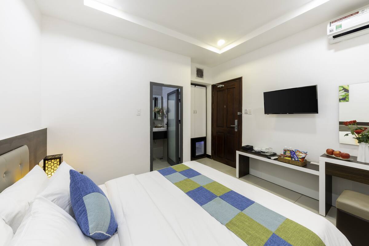 A hotel room with a bed, a desk, a television, and a bathroom visible through an open door.