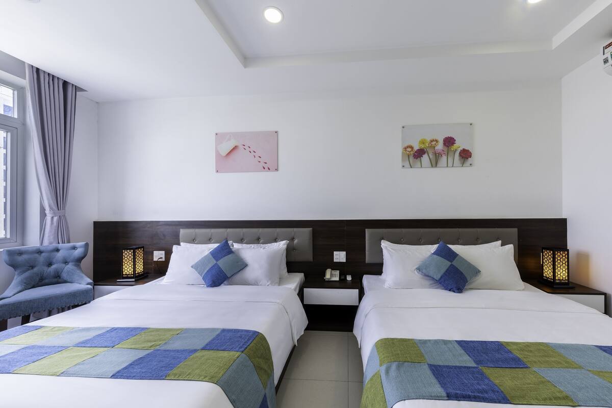 A hotel room with two beds, a nightstand with a phone, a chair, and artwork on the wall.