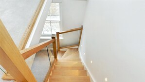 A wooden staircase with glass railings leading to a bright room with a window. - Rainsford Mews by Lime Street (London)