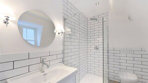 A modern bathroom with a white sink, a round mirror, and a shower area with white tiles. - Rainsford Mews by Lime Street (London)