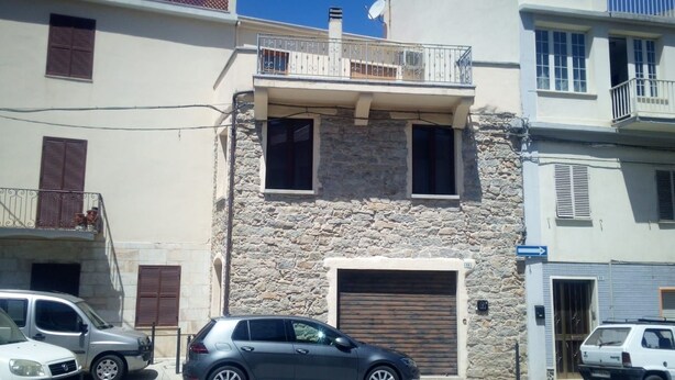 A two-story building with a stone facade, a balcony with metal railings, and a garage door. - B&B Mamoiada Centro (Mamoiada)