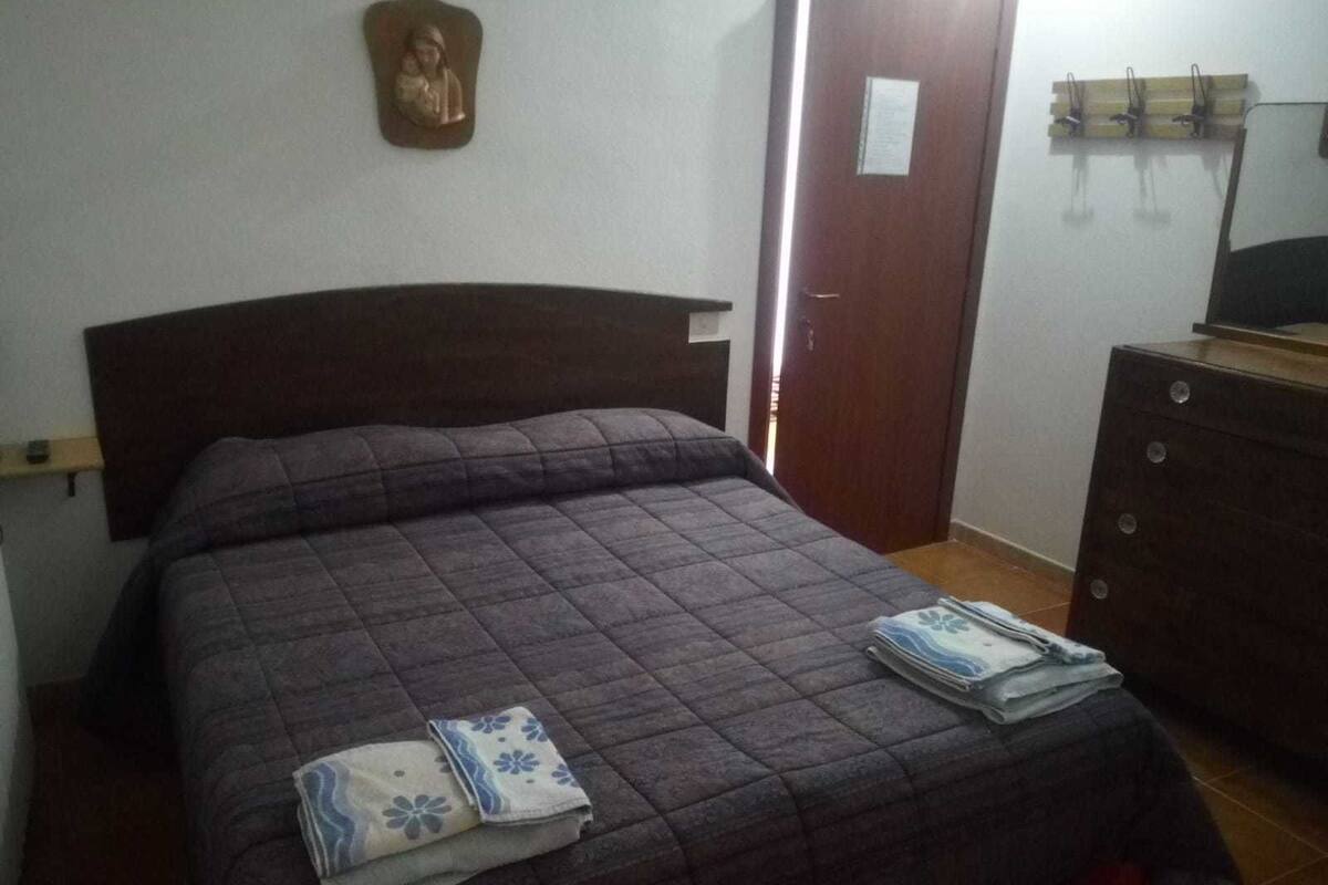 A bedroom with a dark brown headboard, a bed with a quilted cover, and a wooden dresser with a mirror.