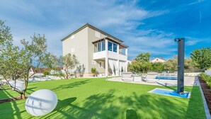 Una casa moderna de dos pisos con balcón, piscina y césped bien cuidado.