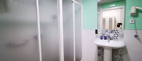 Un baño con lavamanos blanco, baldosas estampadas, un espejo y una puerta con secador de pelo en la pared.