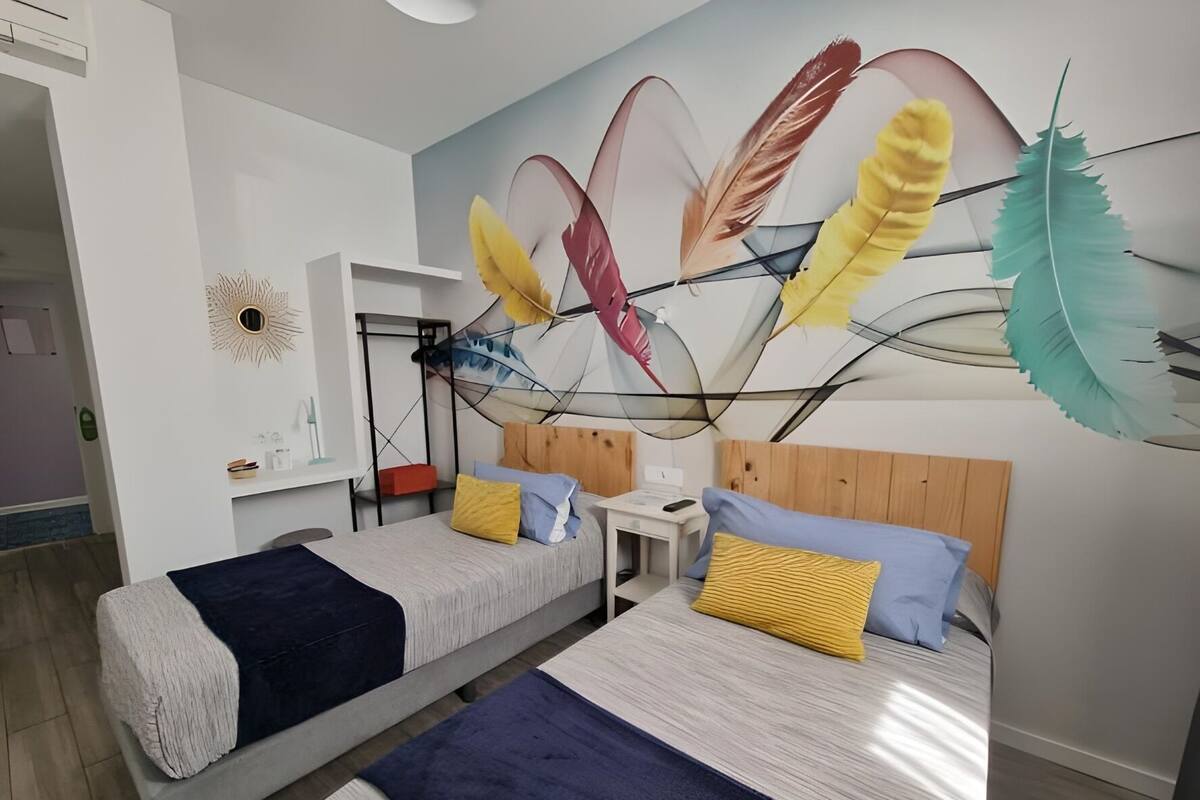 Un dormitorio moderno con dos camas, un escritorio pequeño y un mural decorativo en la pared.