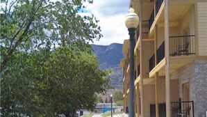 Un hotel de varios pisos con balcones, un camino empedrado y un paisaje montañoso al fondo.