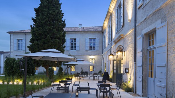 A courtyard with outdoor seating, a large tree, and a building with a light-colored facade and shutters. - Hotel College des Doctrinaires, BW Premier Collection (Lectoure)