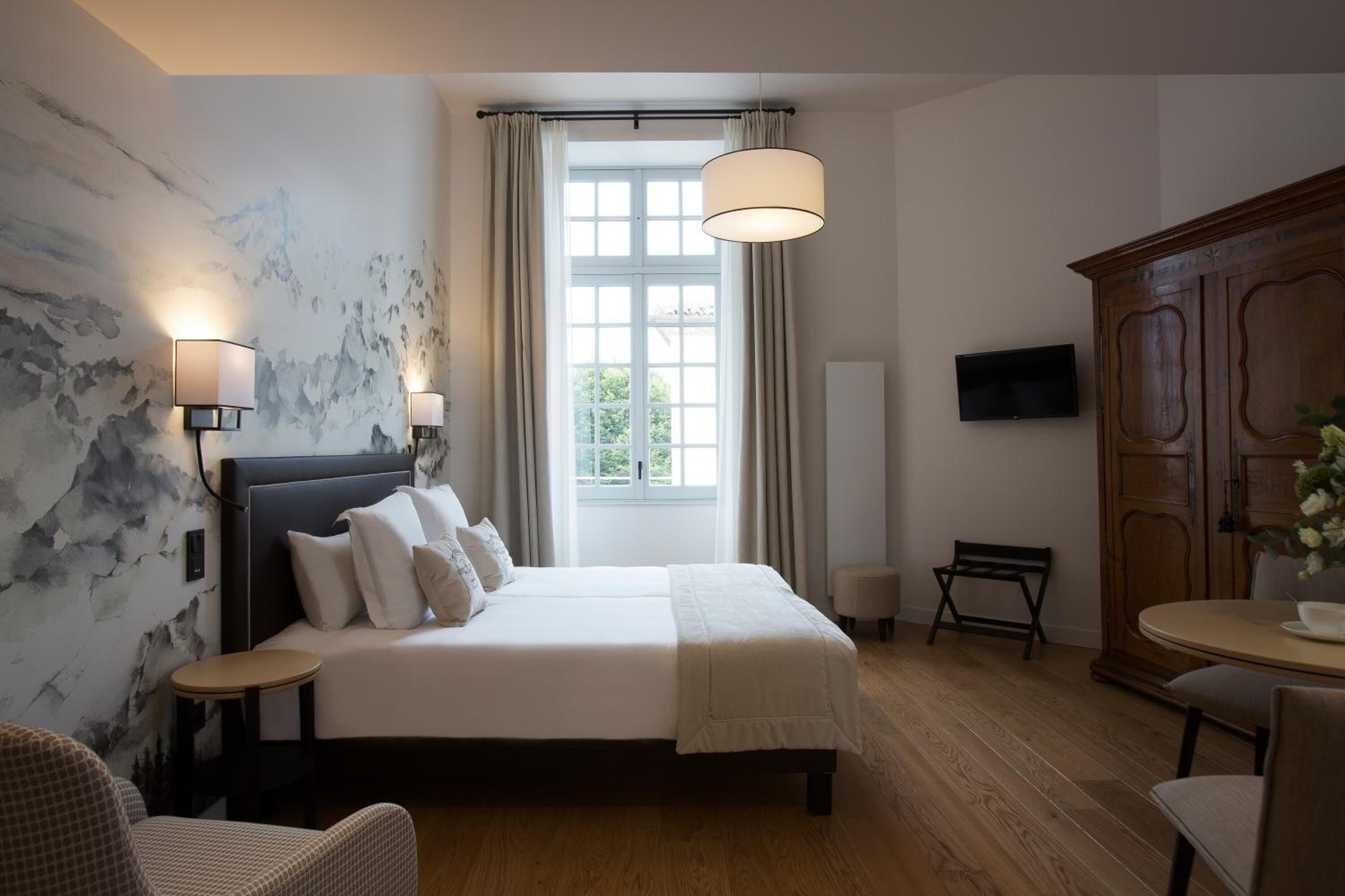Habitación de hotel con una cama grande, dos mesitas de noche, un televisor, un armario de madera y una ventana con cortinas.