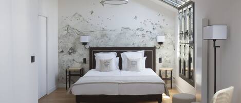A modern bedroom with a large bed, two bedside tables, a chair, a floor lamp, and a view of the sky through a skylight.