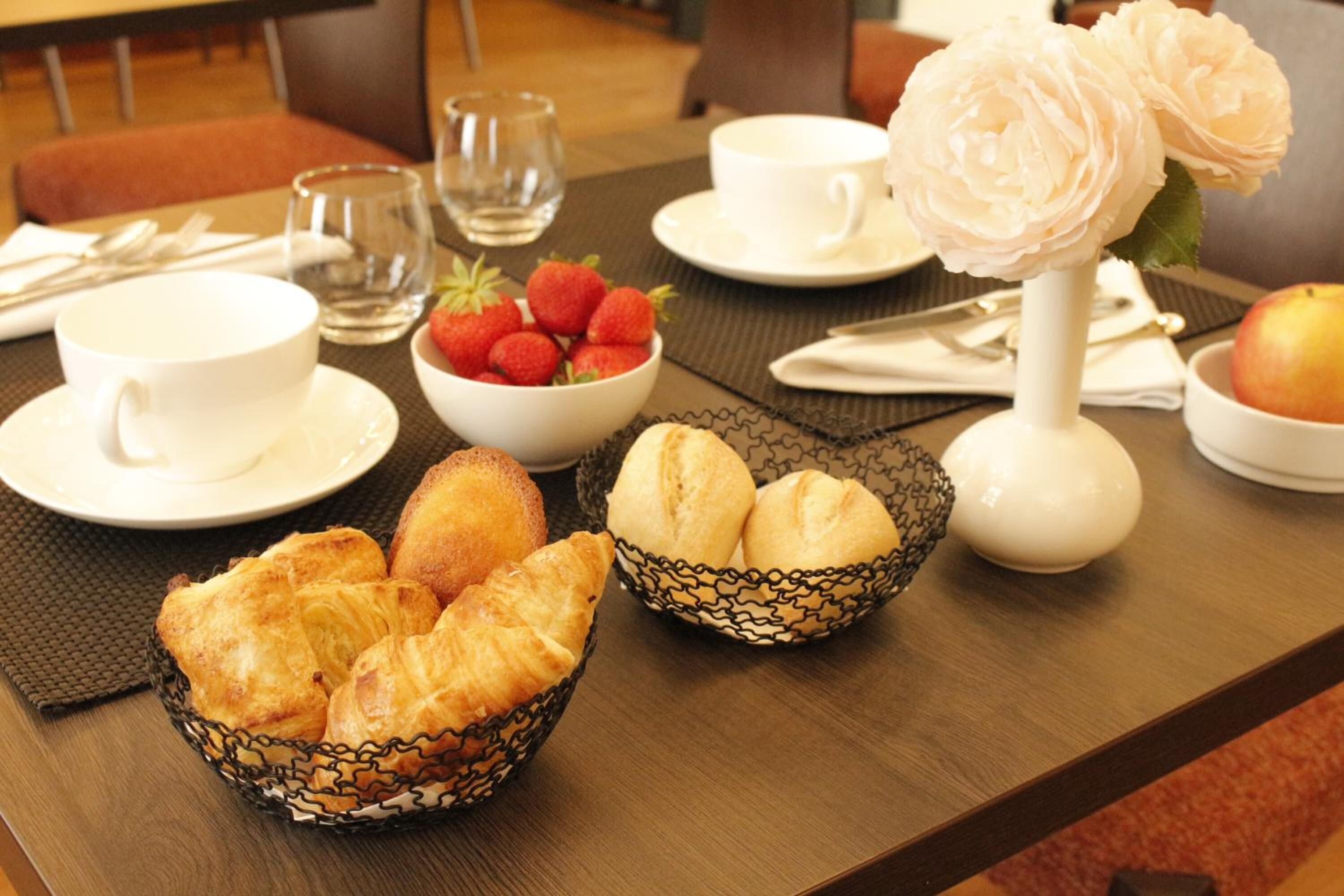 A breakfast setting with croissants, strawberries, and a vase of flowers on a table.