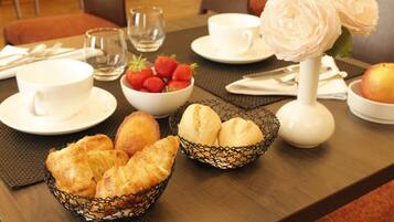 A breakfast setting with croissants, strawberries, and a vase of flowers on a table.