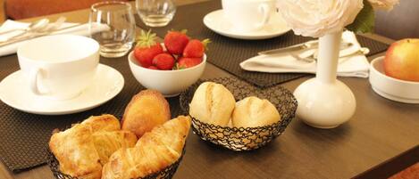 A breakfast setting with croissants, strawberries, and a vase of flowers on a table.