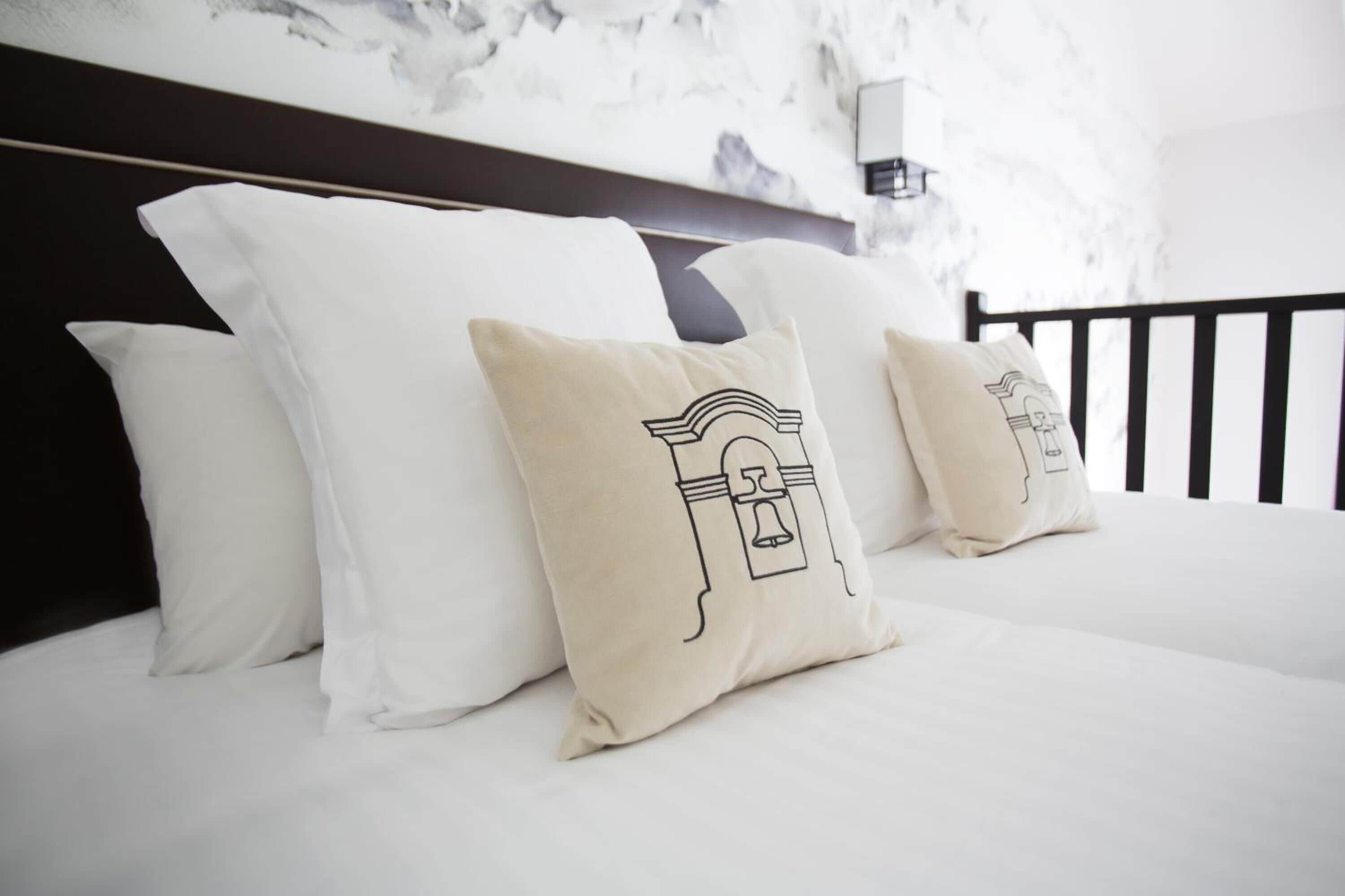 A bed with white bedding and beige pillows with a bell design.