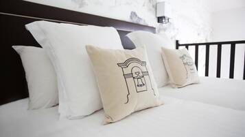 A bed with white bedding and beige pillows with a bell design.