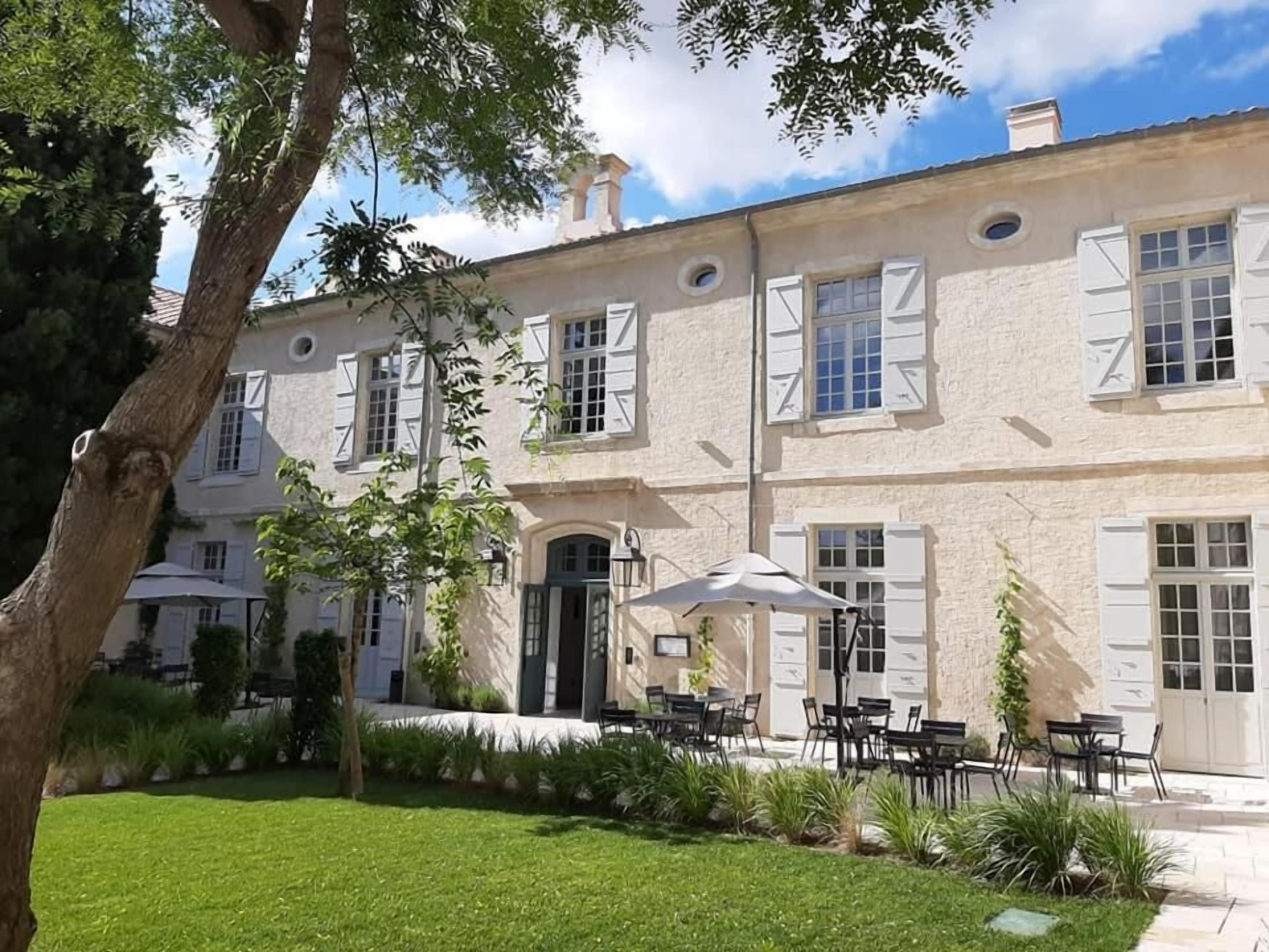 A two-story building with a garden patio area featuring outdoor seating and a large umbrella.