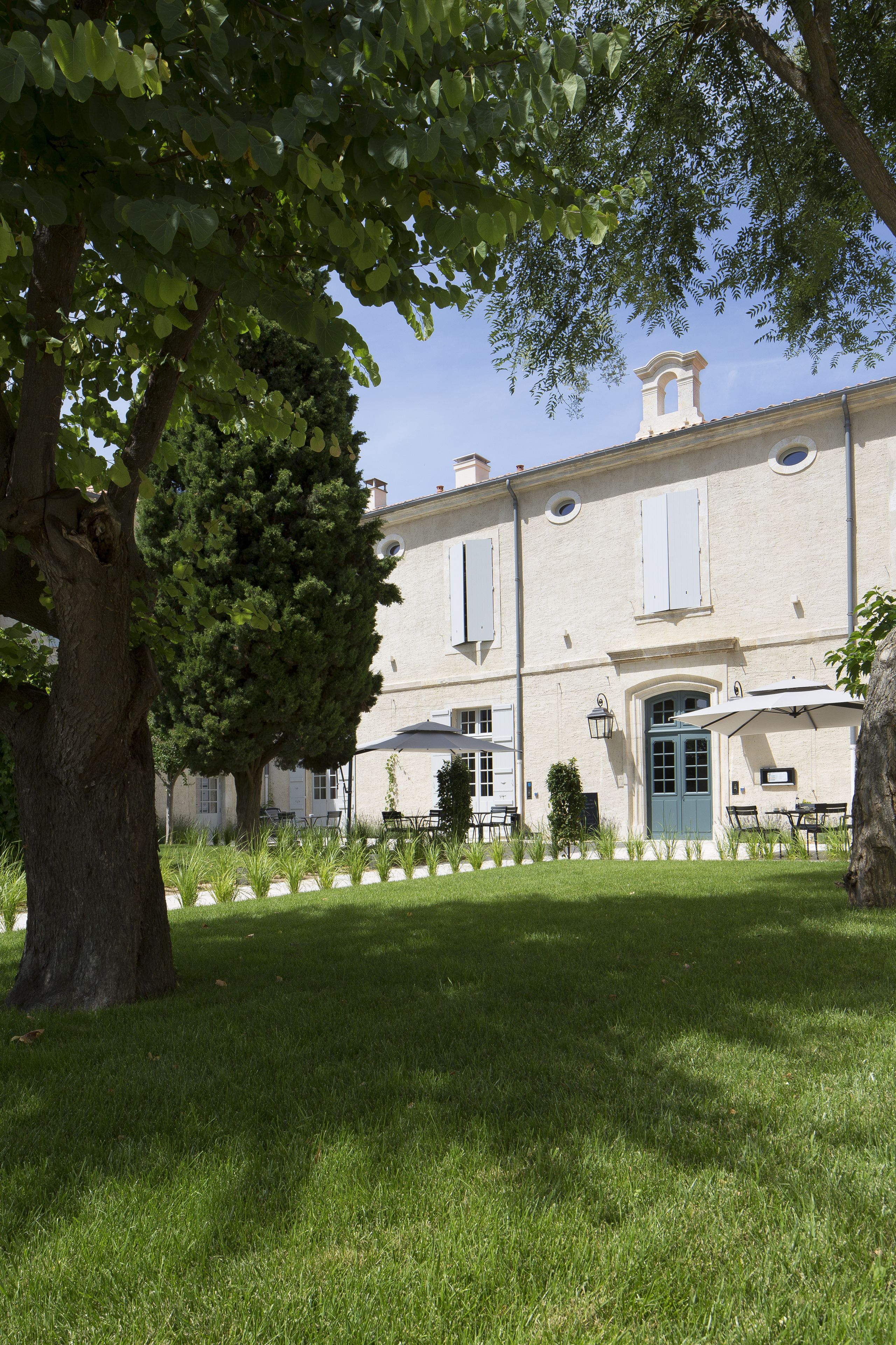 Un bâtiment avec un grand arbre au premier plan, une pelouse bien entretenue et un ciel dégagé.