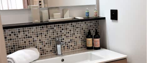 A modern bathroom with a white sink, wooden vanity, and a tiled backsplash.