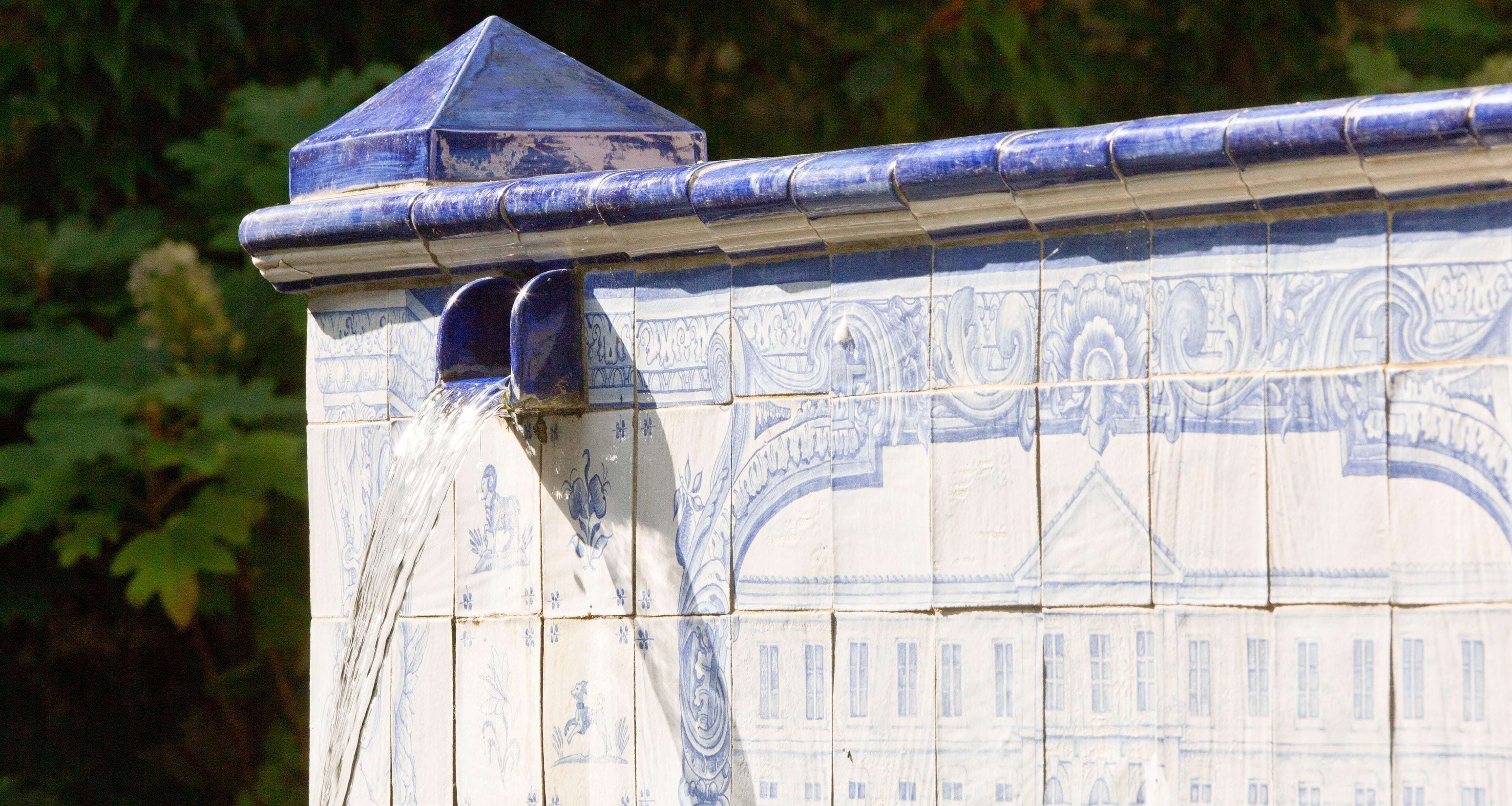 A section of a building with blue and white patterned tiles, a corner with a triangular roof, and a water spout.