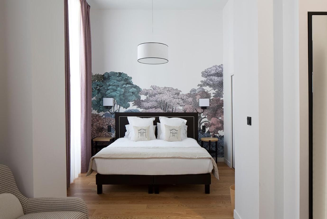 Un dormitorio con cama, mesita de noche, lámpara y un mural en la pared.