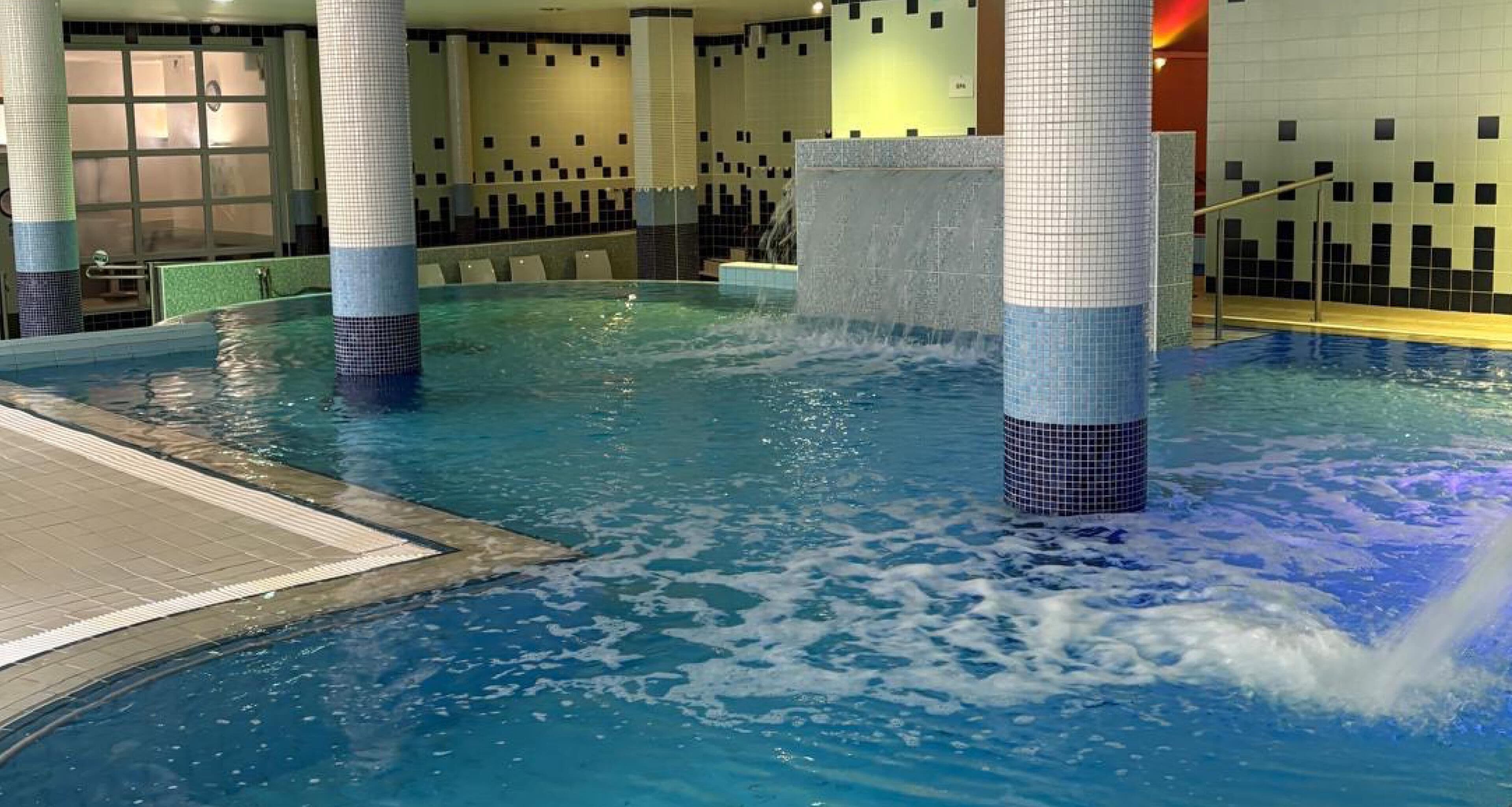An indoor swimming pool with clear water, tiled walls, and a tiled floor.