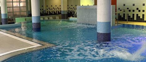 Una piscina interior con agua cristalina, paredes y piso de azulejos.