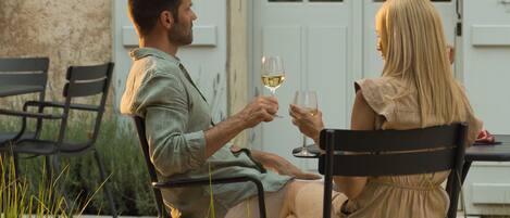 Two people seated at an outdoor table with chairs, holding wine glasses.
