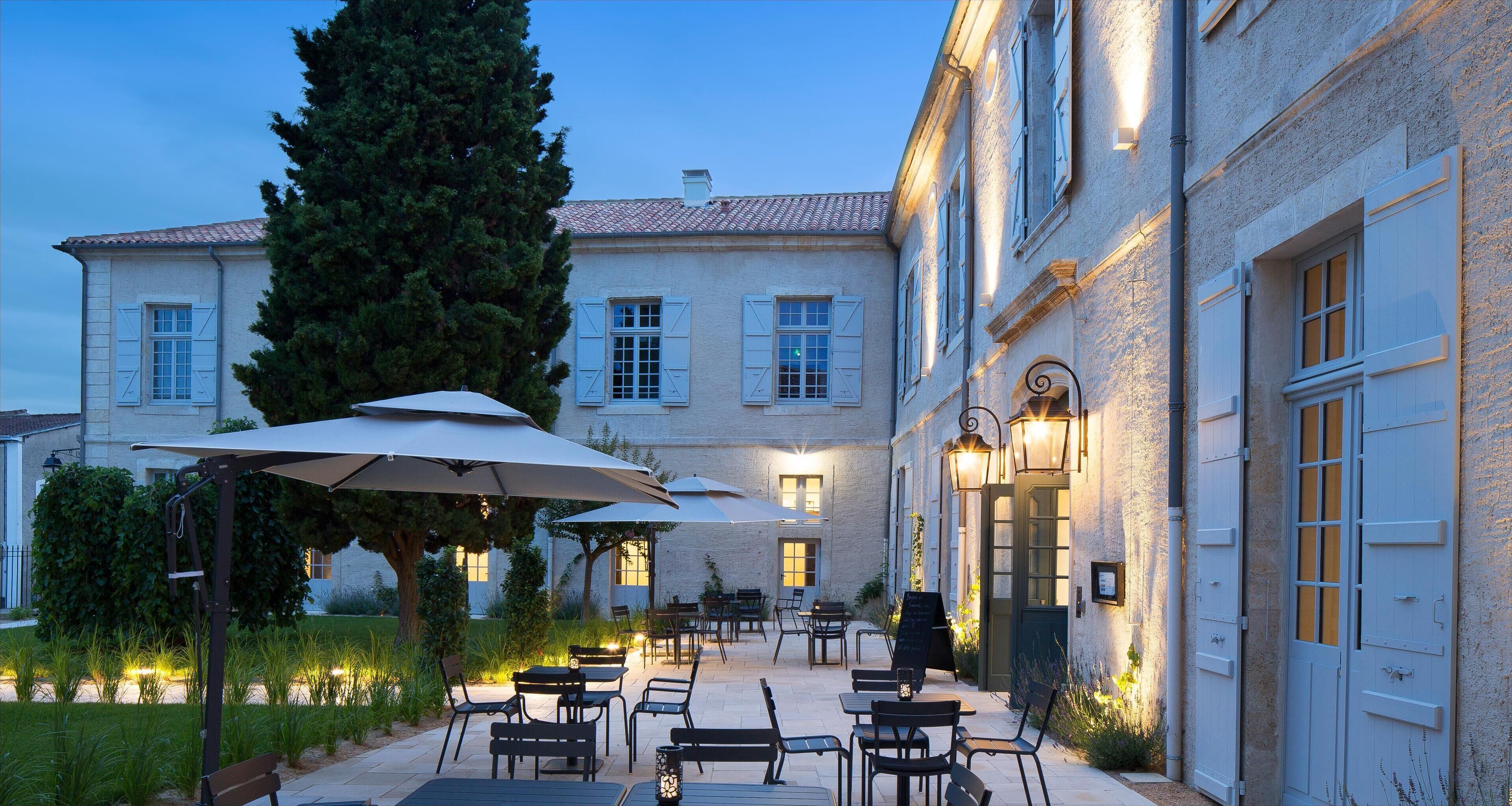 A courtyard with outdoor seating, a large tree, and a building with multiple windows and doors.