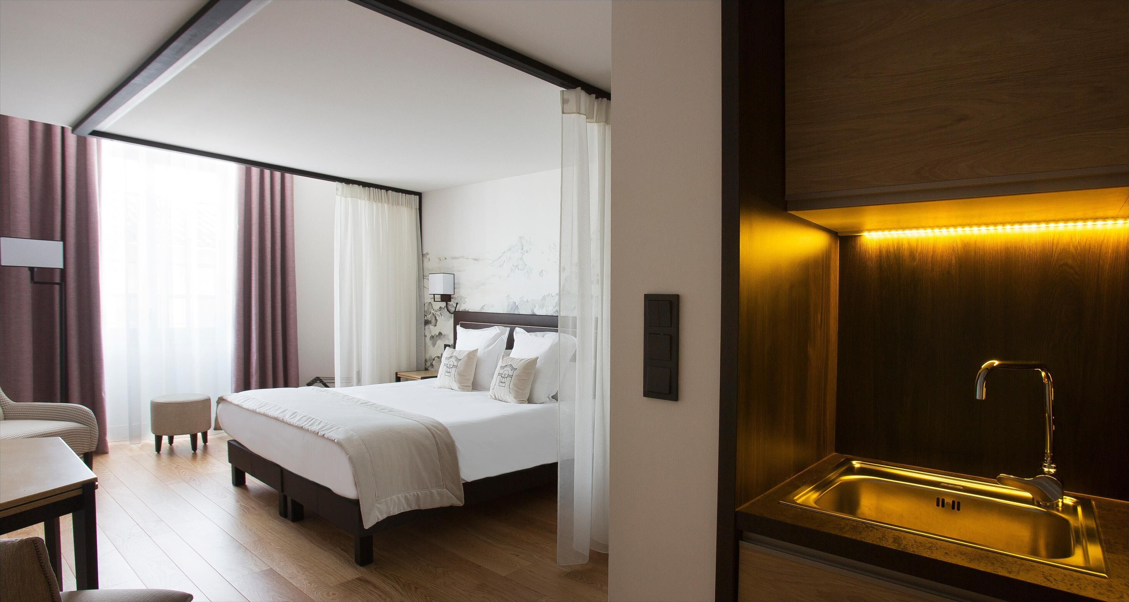 Une chambre d’hôtel comprenant un lit, un bureau, une chaise, une salle de bain avec un lavabo et un luminaire fixé au mur.
