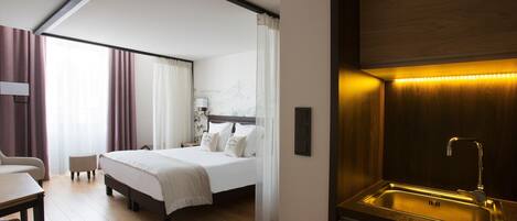 A hotel room with a bed, a desk, a chair, a bathroom with a sink, and a wall-mounted light fixture.