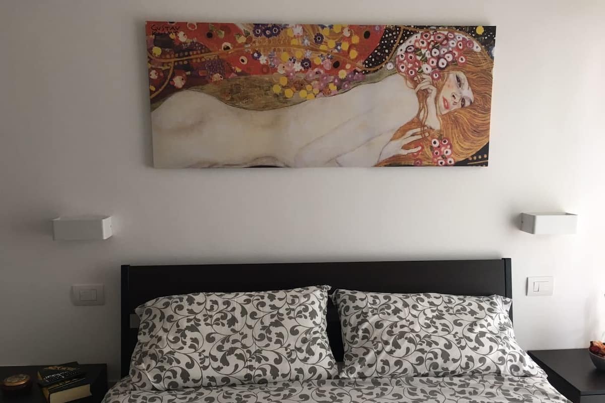 Una cama con ropa de cama estampada, cabecera negra y un cuadro colgado en la pared.