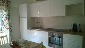 A compact kitchen with white cabinets, a stainless steel oven, and a coffee maker on the counter. - B&B Villa Francesca (Spoltore)