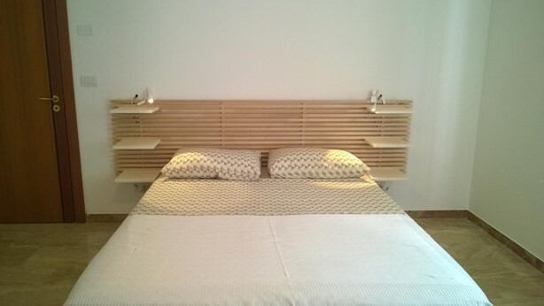 A bedroom with a wooden headboard, a bed with white bedding, and a bedside table with a lamp. - B&B Villa Francesca (Spoltore)