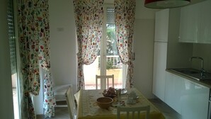 A small kitchen with a dining table set for two, a white refrigerator, and a window with floral curtains. - B&B Villa Francesca (Spoltore)