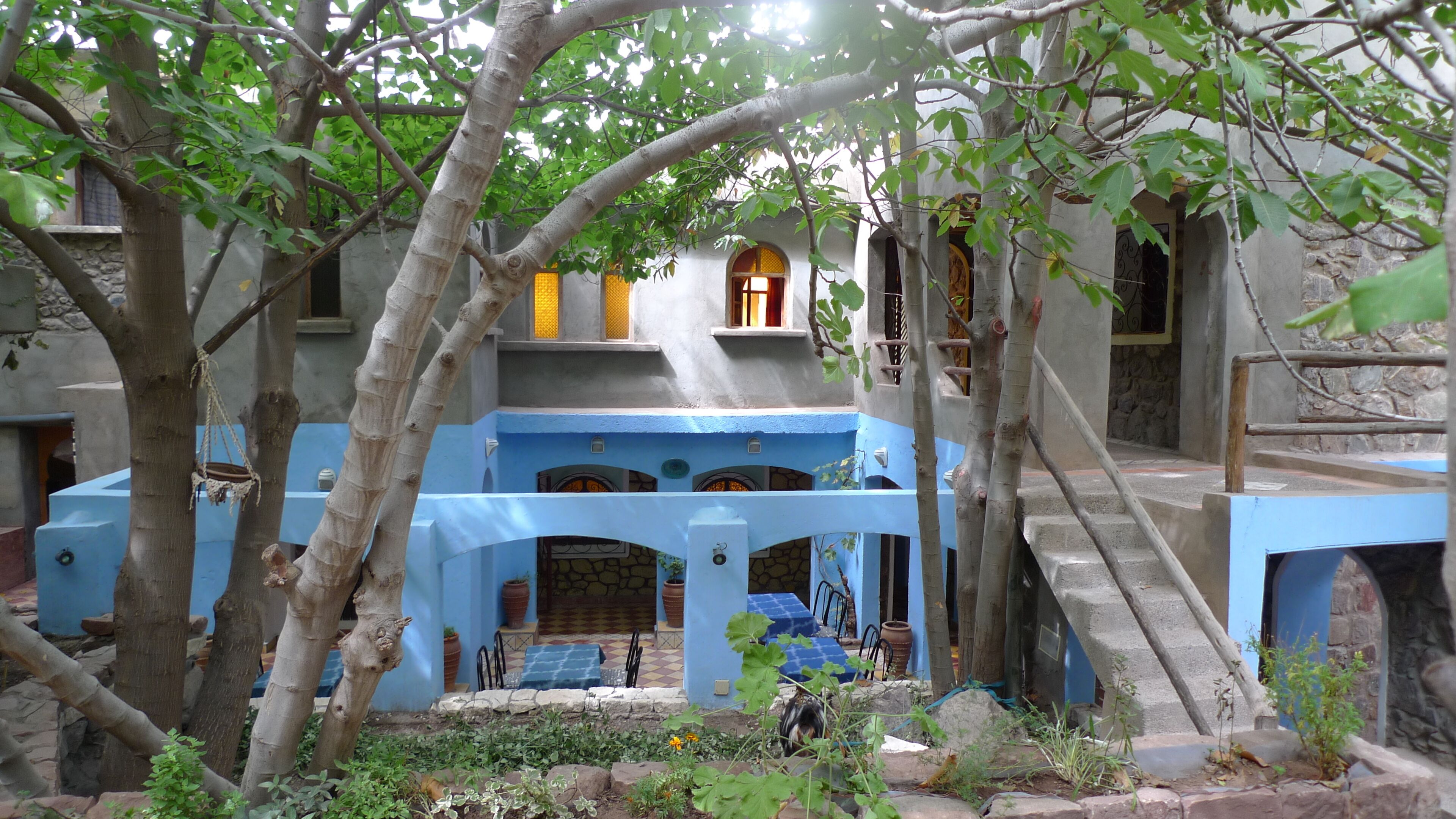 Un patio con un edificio azul, muros de piedra y árboles.