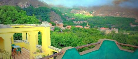 Un edificio amarillo con balcón, que da a un valle con casas y vegetación.
